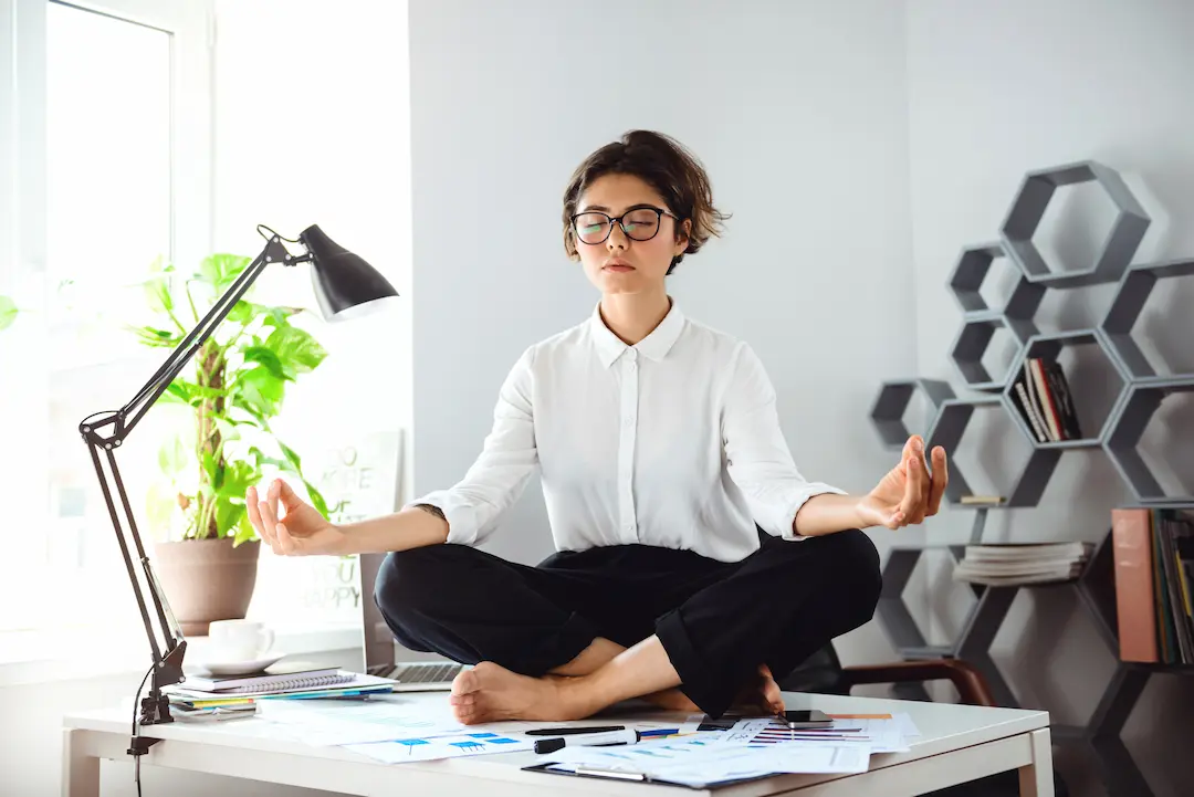 Mujer meditando en la oficina para reducir el estrés postvacacional.