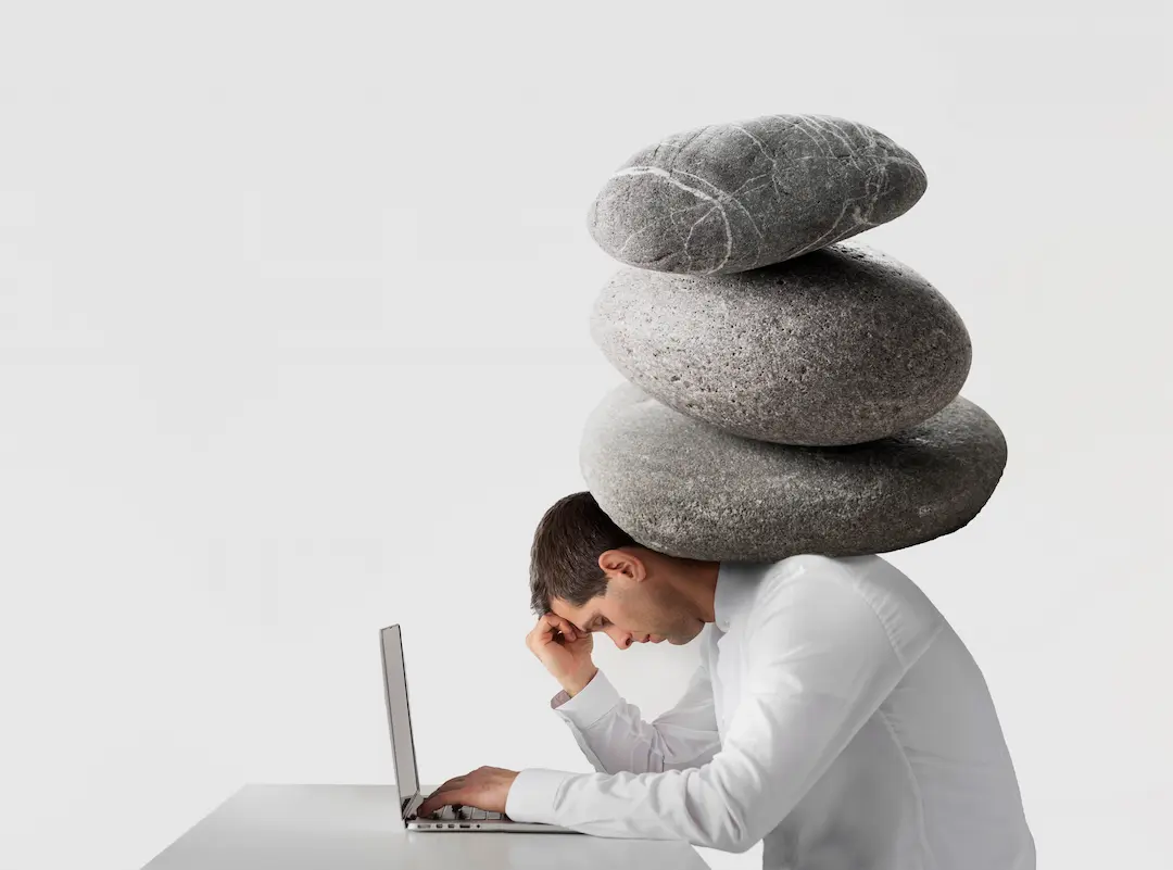 Hombre con piedras sobre la espalda representando la presión del estrés postvacacional.
